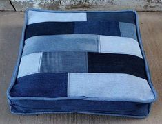 a blue and white patchwork cushion sitting on top of a wooden floor next to a brick wall