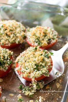 four tomatoes stuffed with cheese and herbs on a cutting board next to a spoon full of seasoning