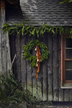 a wreath is hanging on the side of a wooden building with an open window and door