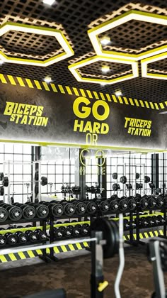 an empty gym with yellow and black lettering on the ceiling, along with rows of dumbs