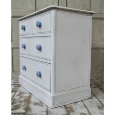 a white dresser sitting on top of a wooden floor next to a wall with blue knobs