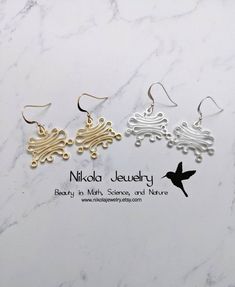 three pairs of earrings sitting on top of a white marble counter with the words, nikola jewelry