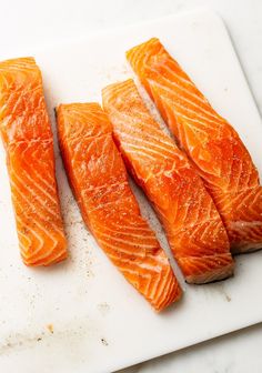 four pieces of raw salmon on a cutting board