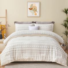 a bed with white comforter and pillows in a room next to a potted plant