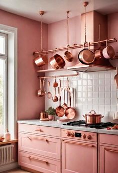 a pink kitchen with copper pots and pans hanging from the rack above the stove