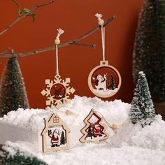 christmas ornaments are hanging from a tree branch in the snow, with santa's house ornament