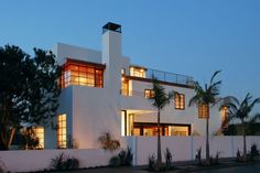 a large white house with palm trees in the front yard at night, lit up by windows