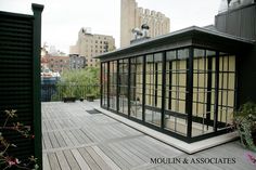 a small building with lots of windows on top of a wooden deck in front of tall buildings