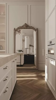 a kitchen with white cabinets and wood flooring next to a large mirror on the wall