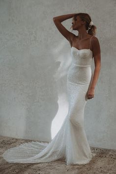 a woman in a white wedding dress standing against a wall with her hand on her head