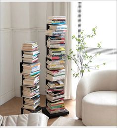 a tall stack of books sitting on top of a wooden floor next to a white couch