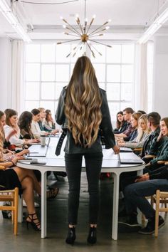 a woman standing in front of a group of people at a table with laptops