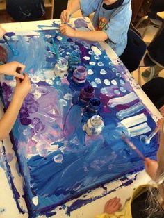 three children are painting on a large sheet of blue and purple paper with watercolors