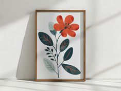 an orange flower with green leaves on a white background in a wooden frame hanging on the wall