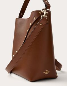 Valentino Garavani Rockstud Wispy bucket bag in calfskin decorated with small studs set on a diagonal. The bag can be worn over the shoulder/crossbody or carried by hand thanks to the adjustable shoulder strap and leather handle. - Platinum-finish hardware - Magnetic closure - Adjustable and detachable leather shoulder strap - Suede lining - Handle drop length: 11 cm / 4.3 in. - Shoulder strap drop length: min. 47 cm to max. 53 cm / min. 18.5 in. to max. 20.9 in. - Dimensions: W18xH20xD10 cm / W Luxury Brown Bucket Bag With Metal Hardware, Designer Brown Bucket Bag With Branded Hardware, Designer Bags With Rivets, Brown Leather Bags With Rivets, Formal Leather Bags With Studs, Designer Leather Shoulder Bag With Studs, Brown Bucket Bag With Metal Hardware, Studded Sneakers, Oxford Boots