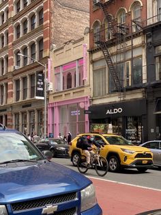 a man riding a bike down a street next to parked cars and tall brick buildings