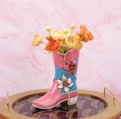 a pink and blue boot with flowers in it on a marble tray against a pink wall