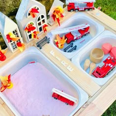 two trays filled with sand and toys on top of a wooden table in the grass