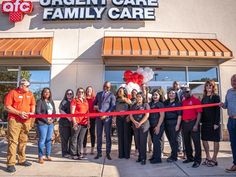 a group of people standing in front of a store with a ribbon cutting the ribbon