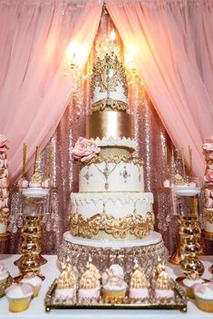 a wedding cake and cupcakes displayed on a table with pink draping