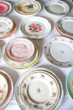 a table topped with lots of plates covered in pink and green flowers on top of white cloth