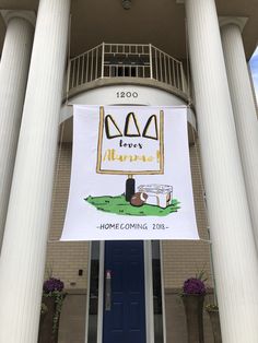 a banner hanging from the side of a building in front of a blue door and some white pillars