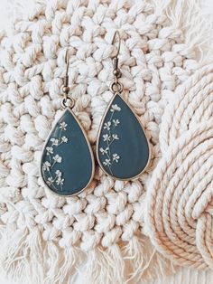 a pair of blue tear shaped earrings with white flowers on them sitting next to a pile of yarn