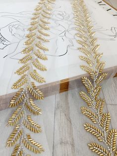 gold and silver beaded leaves are on the edge of a piece of fabric that has been drawn onto