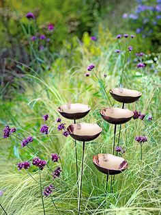 three metal birdbathes sitting on top of tall grass and purple flowers in the background