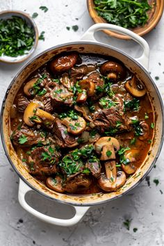 a pot full of stew with mushrooms and parsley in it on a white surface