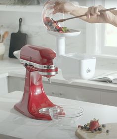 a woman is using a red mixer to mix berries in a bowl on the kitchen counter