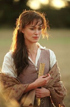 a woman with long brown hair holding a cell phone in her right hand and looking at the camera