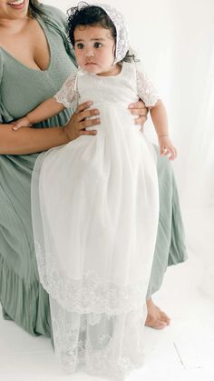 a woman holding a baby wearing a white dress