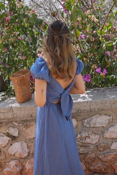 a woman in a blue dress is looking at some pink flowers and trees with her back to the camera