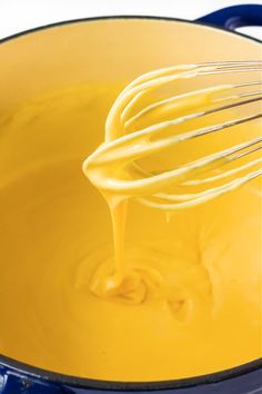 a whisk is being stirred in a blue pot filled with yellow liquid,