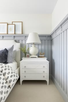 a white bed sitting next to a lamp on top of a dresser in a bedroom