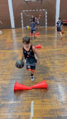 young children playing basketball in an indoor gym with orange cones on the floor and people watching