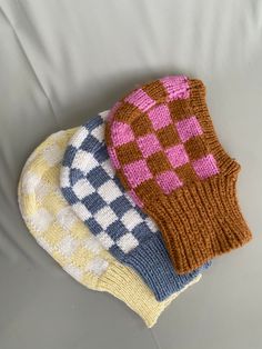 three knitted mittens sitting on top of a white couch next to each other