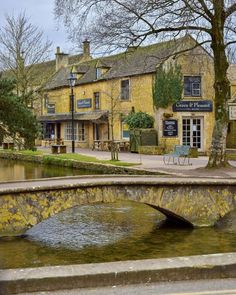 an old stone bridge over a river in front of a yellow brick building with a sign on it