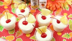 small desserts with pineapple and cherries on a red table cloth next to flowers