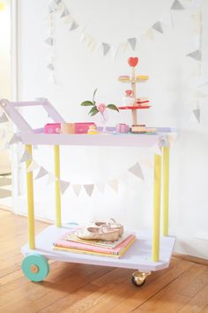 a small cart with books on it in front of a white wall and wooden floor