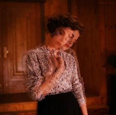 a woman standing in front of a fireplace with her hands on her chest and looking down