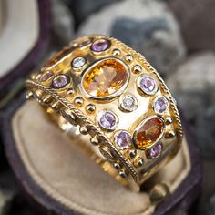 This wonderful wide band cocktail ring is accented with three (3), bezel set, oval mixed cut natural spessartite garnets, twelve (12), bezel set, round brilliant cut natural pink sapphires and six (6), bezel set, round brilliant cut diamonds. The ring measures 17.0mm at the top, rises 5.8mm above the finger, tapering to 4.9mm wide and 1.1mm thick at the base of the shank. This ring is currently a size 10. Purple Garnet, Spessartine Garnet, Gemstone Wedding Rings, Multicolor Jewelry, Spessartite Garnet, Wide Band Ring, Aquamarine Jewelry, Wide Band Rings, Rocks And Gems