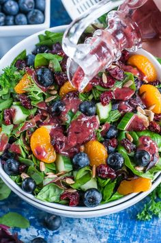 someone pouring dressing onto a salad with oranges, blueberries and cucumbers