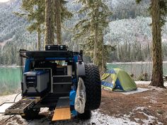 an off - road vehicle parked next to a tent in the woods near a lake