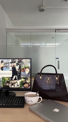 a laptop computer sitting on top of a wooden desk next to a purse and coffee cup