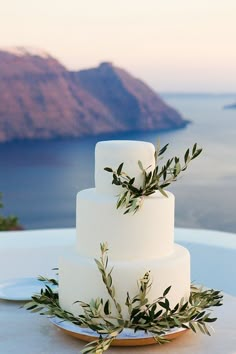 a three tiered white cake sitting on top of a table next to the ocean