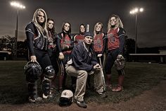 a group of women in baseball uniforms posing for a photo on the field at night