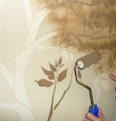 a person painting a wall with a paint roller in front of it and a tree painted on the wall