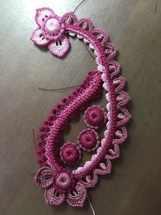 a pink crocheted necklace with flowers on it sitting on top of a table